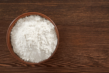 Fototapeta na wymiar Bowl with wheat flour on wooden background, top view