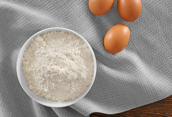 Bowl with wheat flour and raw eggs on table, top view