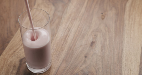 pour strawberry yogurt into glass on wood table