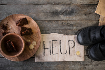 Piece of cardboard with word HELP, old shoes and bread on wooden background