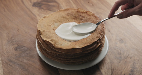 spreading sour cream on top of pancakes or blini