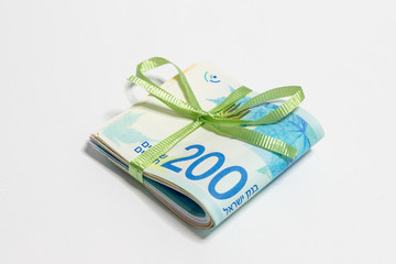 A stack  of folded new Israeli banknotes of different value in shekels (NIS)  tied with green...
