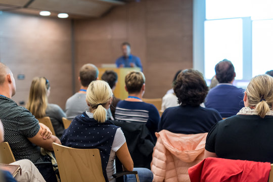 Business and entrepreneurship symposium. Speaker giving a talk at health care workshop meeting. Audience in conference hall. Rear view of unrecognized participant in audience.