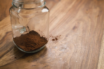 making cocoa drink in glass jar with handle on wood table, adding cacao powder