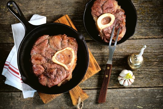 Roast beef shank in a cast-iron frying pan on a wooden background.