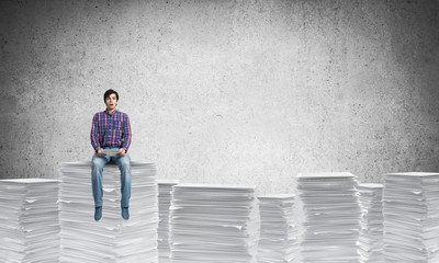 Attractive man sitting on pile of paper documents.