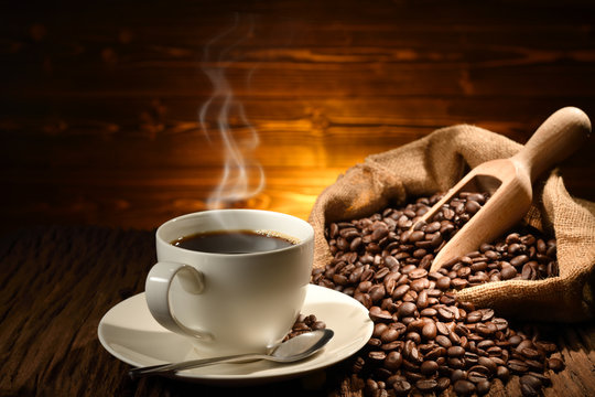 Fototapeta Cup of coffee with smoke and coffee beans on old wooden background