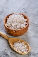 Large white sea salt in a natural wooden bowl on light background, top view, close-up, selective focus