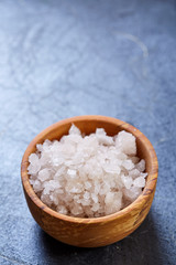Large white sea salt in a natural wooden bowl on dark background, top view, close-up, selective focus