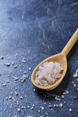 Crystal sea salt in a wooden spoon on dark background, top view, close-up, selective focus.