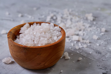 Large white sea salt in a natural wooden bowl on light background, top view, close-up, selective focus