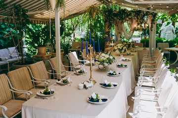 Beautiful and exquisite decoration of the wedding celebration in in the middle of a green garden. Banquet served table with a beige tablecloth, plates and candlesticks with blue candles under cover