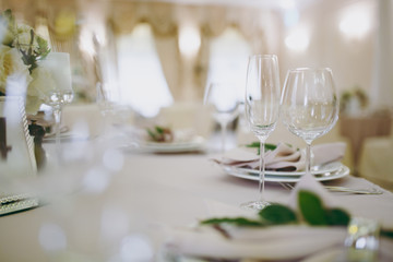 Beautiful decoration of a wedding banquet in a restaurant in pastel colors. Serving the table with beige tablecloth, plates, glasses, cutlery, napkins decoration with a green twig