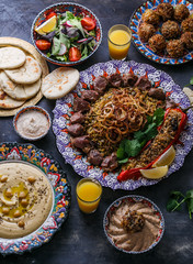 Middle eastern or arabic dishes and assorted meze on a dark background. Meat kebab, falafel, baba ghanoush, hummus, rice with vegetables, tahini, kibbeh, pita. Halal food. Space for text. Top view