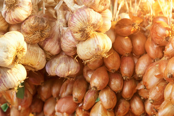 Close up of hanging garlic bulbs and white onions with selective focus and sunlight from behind and space for text.