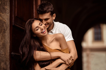 Obraz na płótnie Canvas Happy young female with long dark hair glad to recieve passionate kiss from her boyfriend. Handsome male embraces his girlfriend and kisses. Portrait of lovely young couple express mutual love.