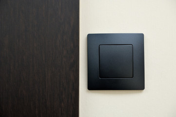 A modern light switch made of black plastic next to the entrance door