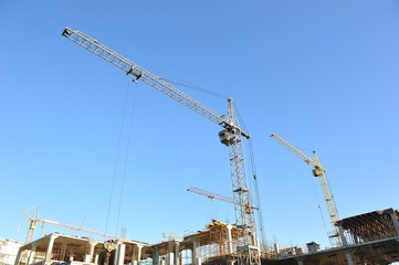 Fototapeta na wymiar Construction cranes on the construction of a large house on a blue sky background
