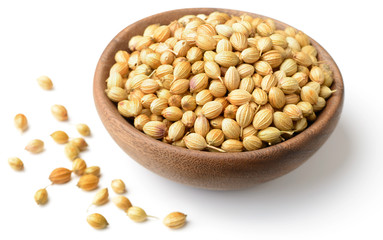 dried coriander seeds in the wooden plate, isolated on white