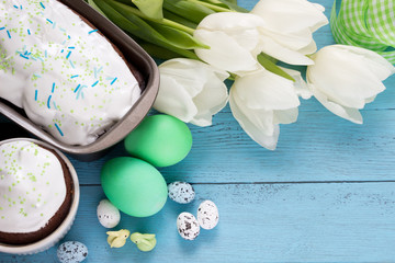 Easter holiday concept-Easter cakes,Easter eggs,bunnies,white tulips and green ribbon on blue wooden board.Template for greeting cards.