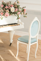 White grand piano with chair near and roses over the instument on the wooden floor in classic interior