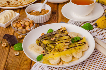 Crepes or pancakes with chocolate cream, bananas and hazelnuts for breakfast