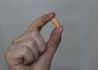 A pill in a woman's hand against a gray background. Close-up. The concept of medicine.