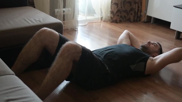 Athletic young man doing Indoor sit ups exercise for abdomen at home.