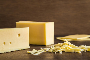 Fresh, yellow cheese with grated slices on the rustic brown wooden table in the kitchen. Farm's natural dairy product. Healthy food. Empty place for text or a logo.