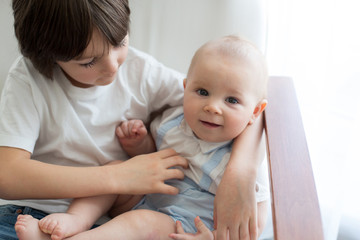 Adorable preschool child, hugging his baby brother in rocking chair