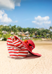 Straw hat, bag, sun glasses and flip flops on a tropical beach