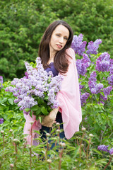 Beautiful young girl with a bouquet of lilacs in the garden