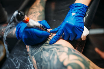 Tattooist makes tattoo by machine on male shoulder