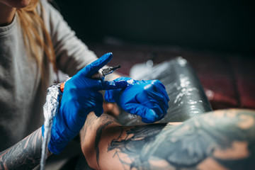 Tattooist makes tattoo by machine on male shoulder