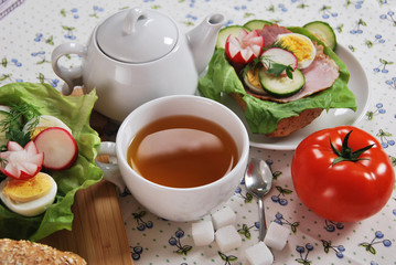 red tomato and sandwich with ham salad with egg and radish with hot tea for a healthy breakfast