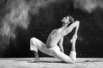 A man doing yoga in a white cloud of dust in a dark room. The concept of energy. Black-and-white photo.