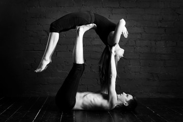 Young Caucasian yoga couple. Sporty handsome man supports and holds a slender girl. yoga concept shows strength and trust. black-white