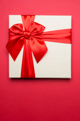 White gift box with red ribbon on red isolated background