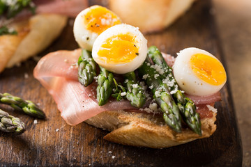 Fresh sendwich with ham, asparagus and quail eggs on old wooden chopping board. Easter spring...