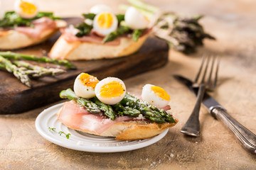 Easter breakfast or lunch with sendwich with ham, asparagus and quail eggs on old wooden chopping board. Spring food concept with copy space.