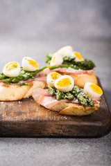 Easter breakfast or lunch with sendwich with ham, asparagus and quail eggs on old wooden chopping board. Spring food concept with copy space.
