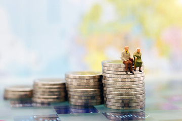 Miniature people: Happy senior couple sitting on coins stack, money saving growth. Retirement, ...