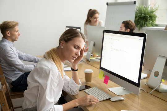 Stressed overwhelmed young businesswoman feels tired from computer office work, exhausted female employee suffering from headache touching temple at workplace, stress at work or migraine concept