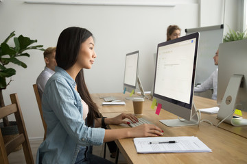 Young asian businesswoman working online on pc desktop computer in modern multiracial office,...