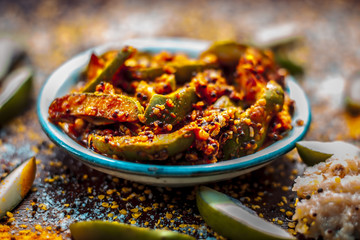 Close up of Aam ka achar or kari ka achar with all its ingredients and speiceis on a wooden surface in drak Gothic colors.