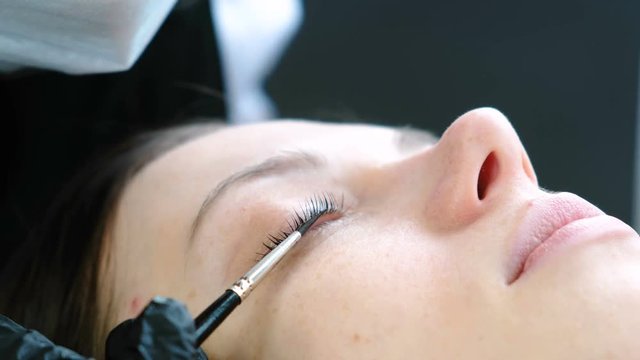 Cosmetologist rubs the client's eyelash with brush. Botox and lash lamination. Closeup eyes.