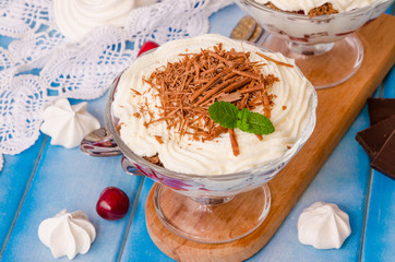 English trifle with chocolate biscuit, whipped cream, cherry and meringue in glass