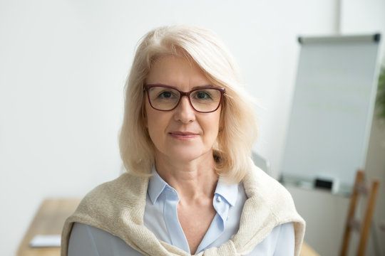 Confident aged businesswoman wearing glasses looking at camera, skilled experienced senior female professional, mature lady teacher coach posing in office alone, older woman boss head shot portrait