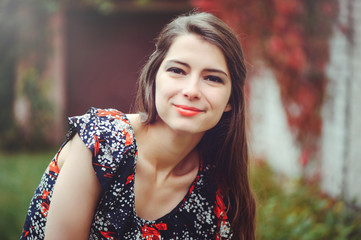 Smiling young brunette woman posing in the courtyard of her residence in dress rejoices, portrait happy carefree, health