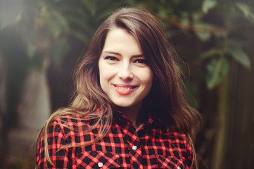 Smiling young brunette woman posing in the courtyard of her residence in a red checkered shirt is happy, portrait of happy carefree, health